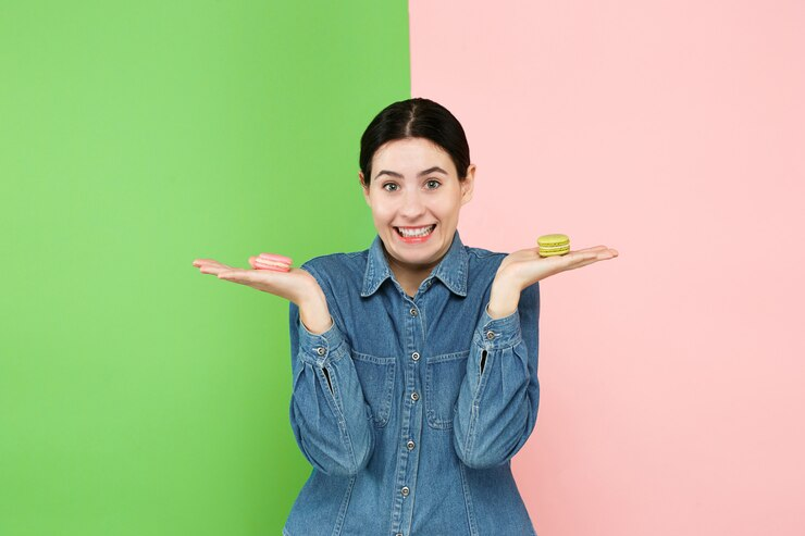 Young excited woman holding macarons in her hands in front of a pink and green plain background