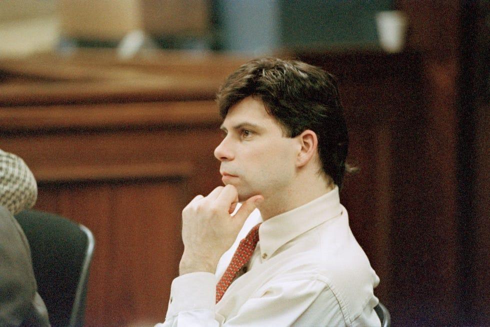 lyle menendez, wearing a white collar shit and red tie, sits with his hand on his chin and listens in a courtroom