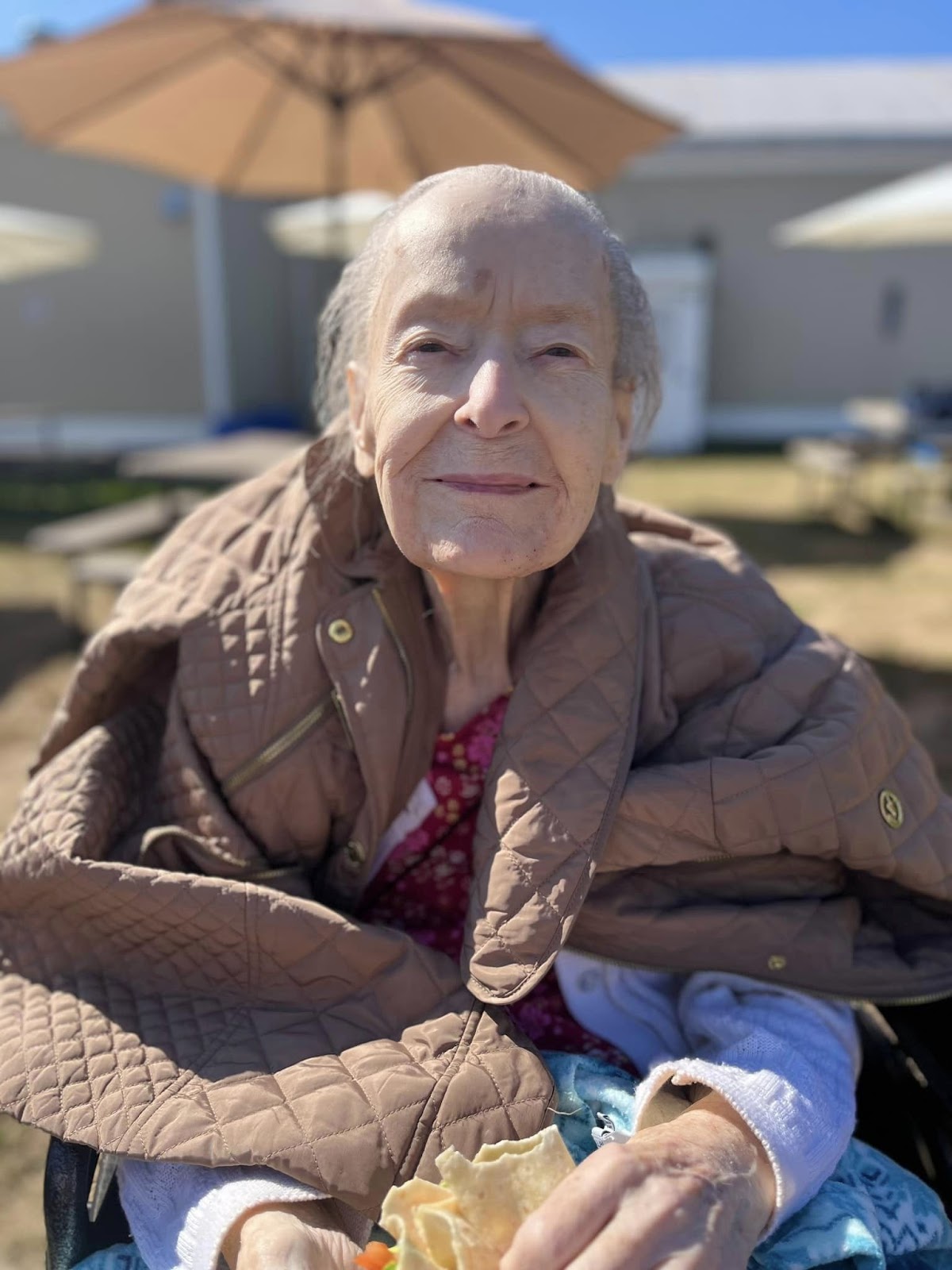 An assisted living resident smiling at the camera while sitting in the sun outdoors