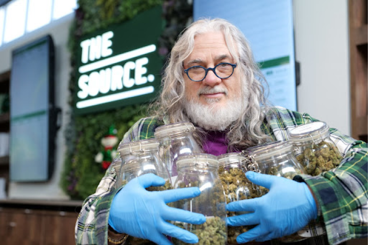 A long, silver-haired gentleman with glasses and a white beard shows his love for cannabis, hugging several jars full of marijuana to his chest.