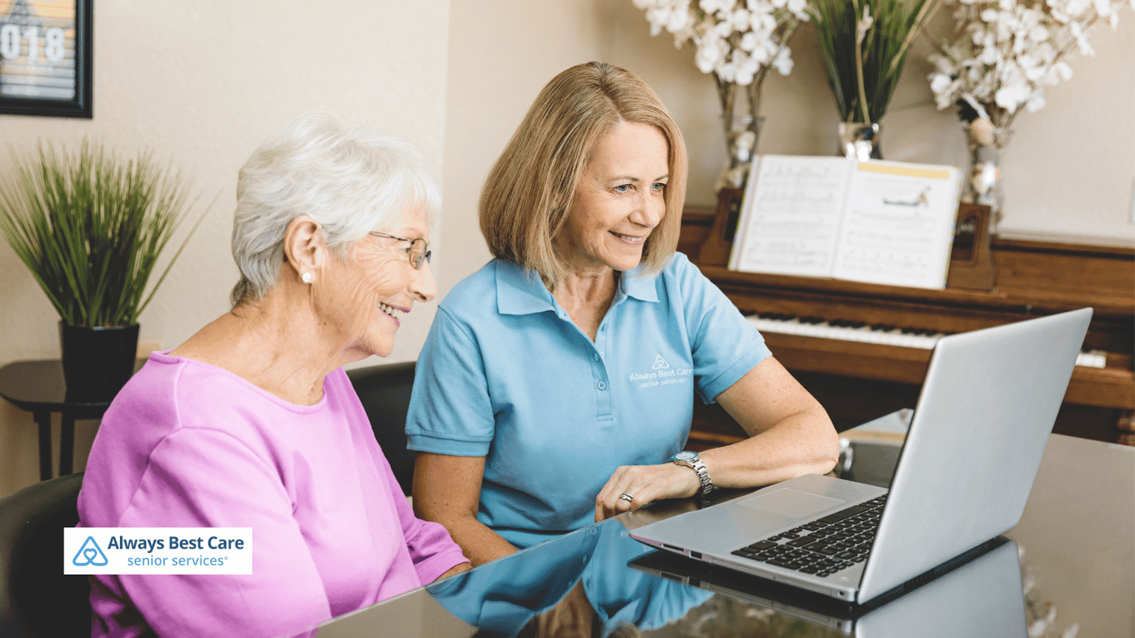 This image depicts a senior woman and a female caregiver looking at a laptop screen