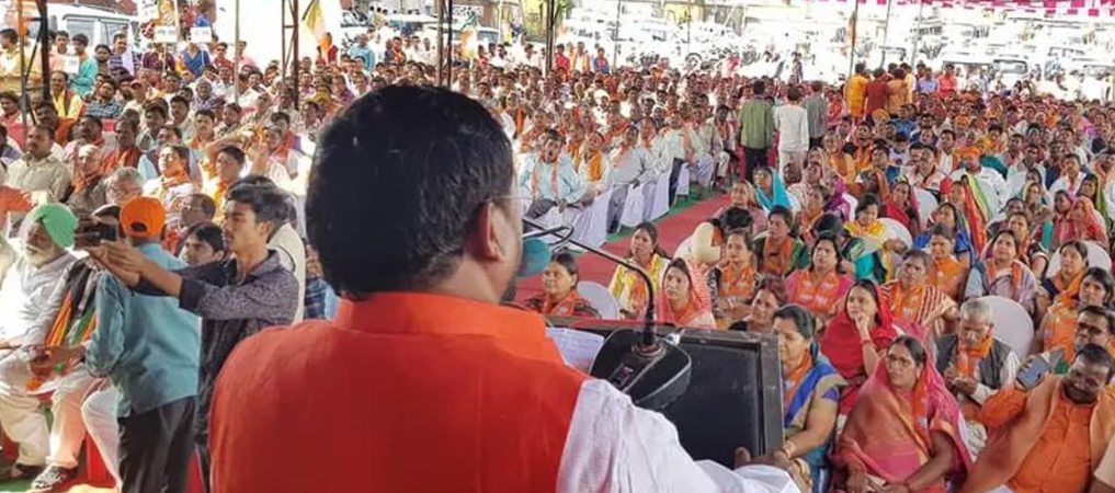 A person in orange shirt speaking into a microphone

Description automatically generated