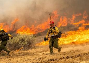 A firefighter running through a field with fire behind him

AI-generated content may be incorrect.