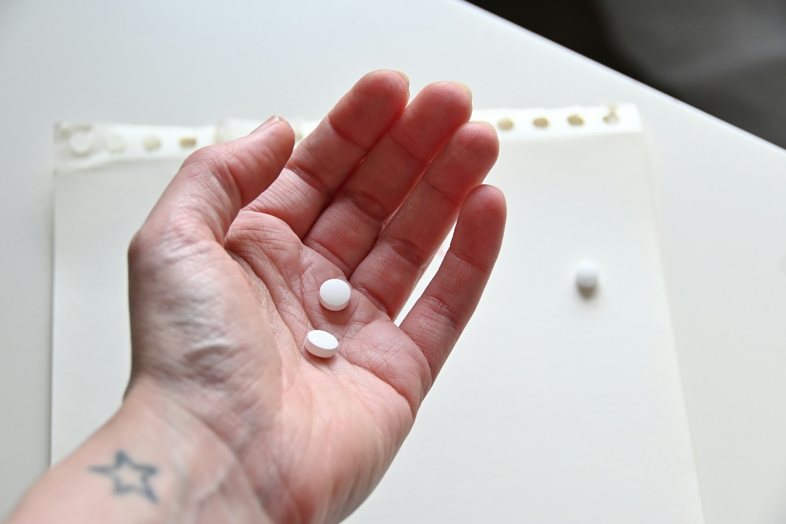 A man holding his hand open with two white medication pills in his palm