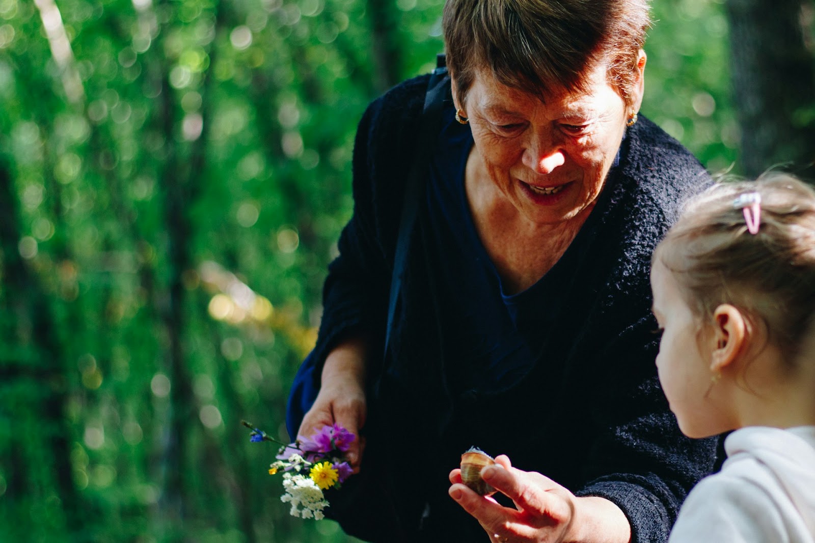 An older woman and a young girl exploring a lush green forest, surrounded by tall trees