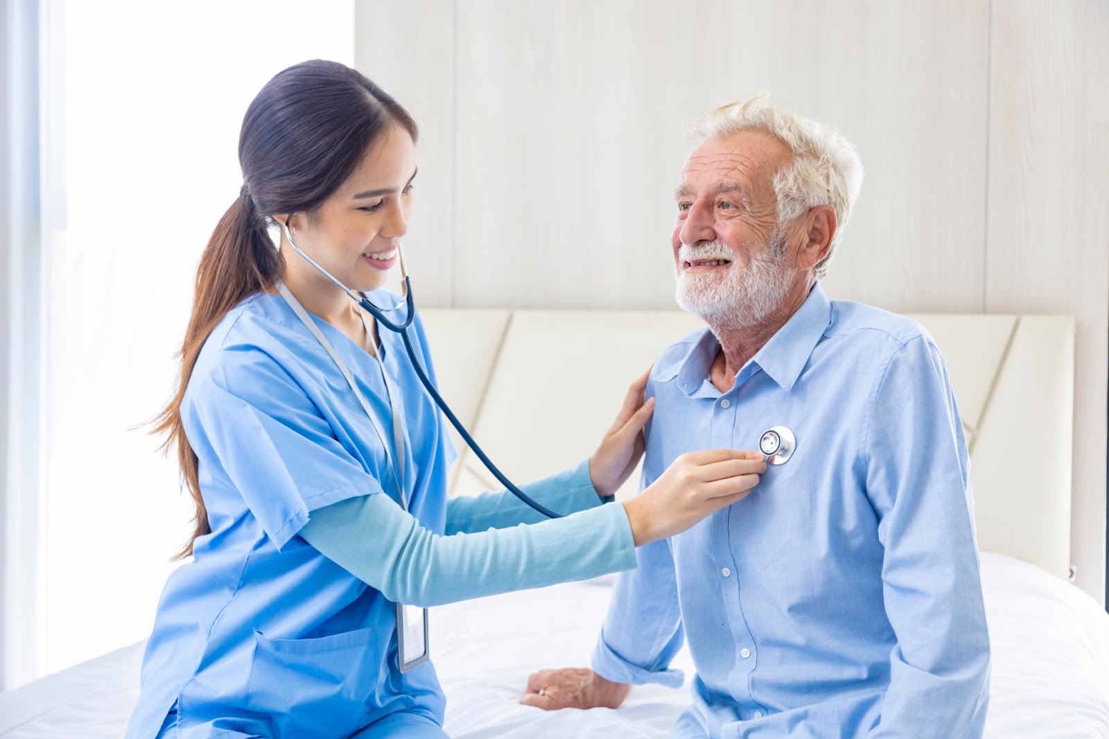 A young Asian caregiver using a stethoscope on a senior man.