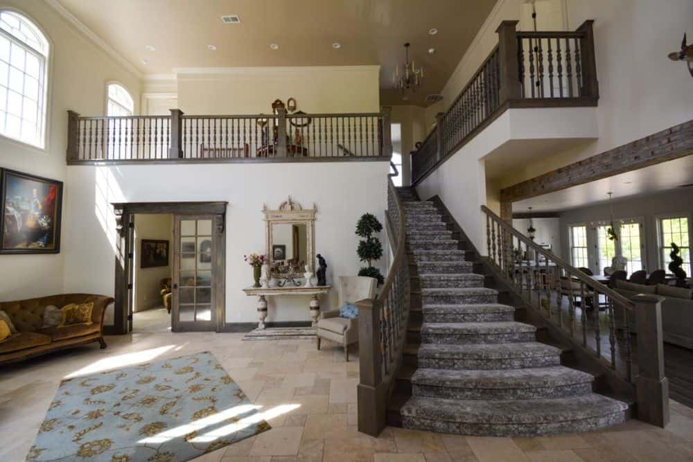 Great room with tufted seats, a floral rug, and a distressed console table. A carpeted staircase serves as a divider between the great room and family room.