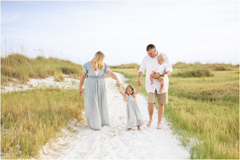 Young family walking barefoot along a sandy path in Anna Maria Island during a golden-hour family portrait session with Love and Style Photography.