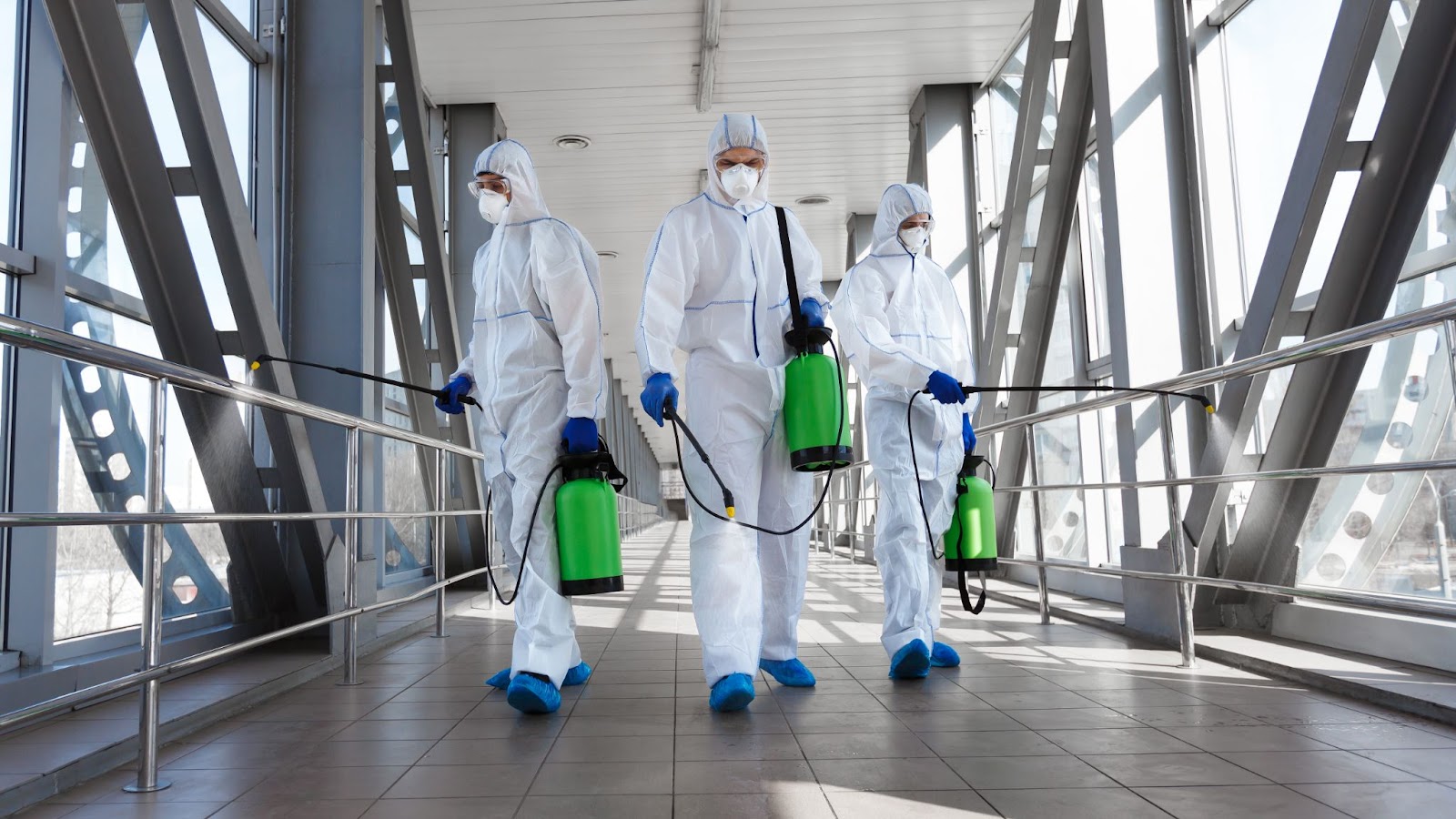 Pest control team in protective suits and masks disinfecting an indoor area with professional equipment.