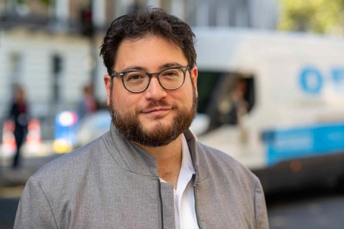 David Tze wearing grey jacket, white shirt, city in the background