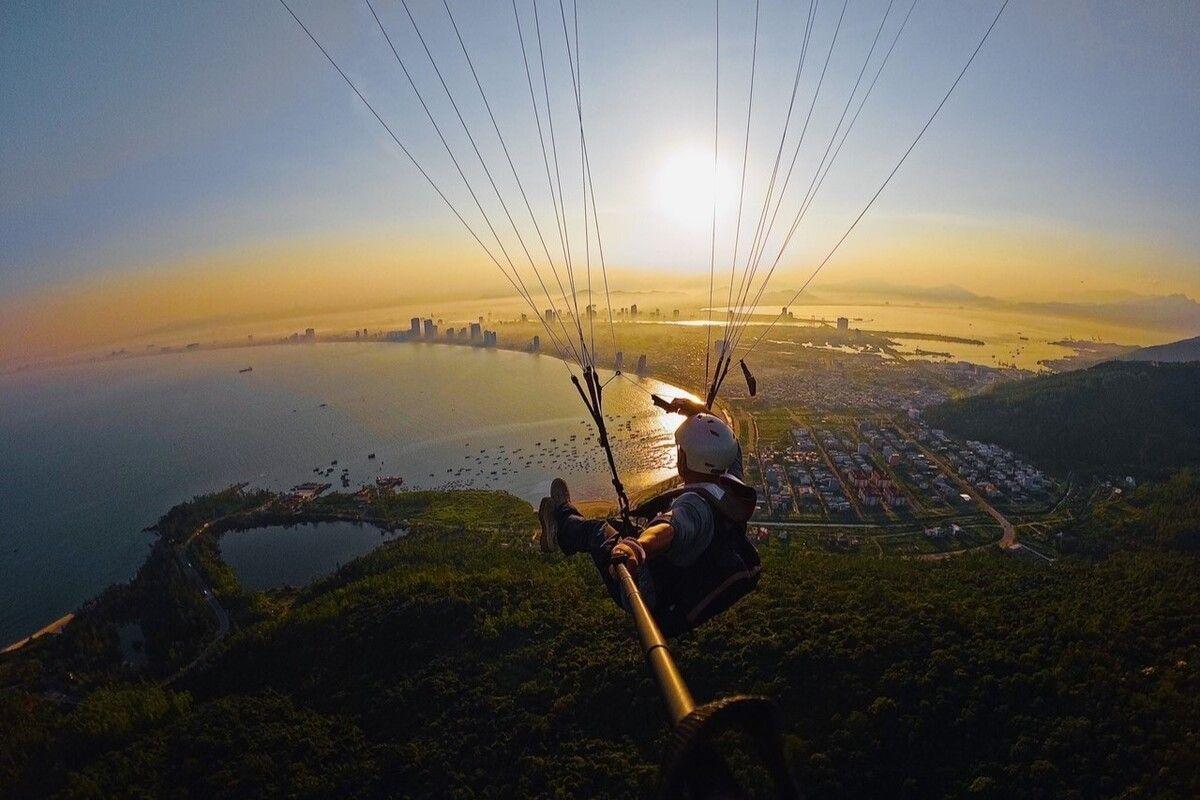 A person in a paraglider flying over a city

Description automatically generated