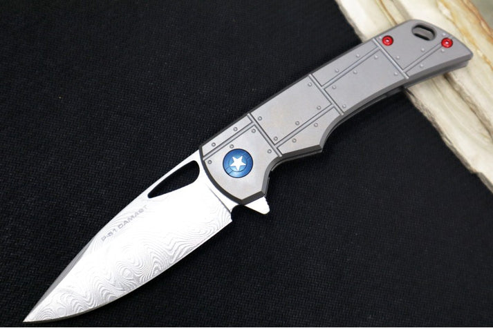 An image showing a modern folding knife from Boker, the Boker Plus P-51 Damascus. The knife features a spearpoint blade and full titanium handle scales.