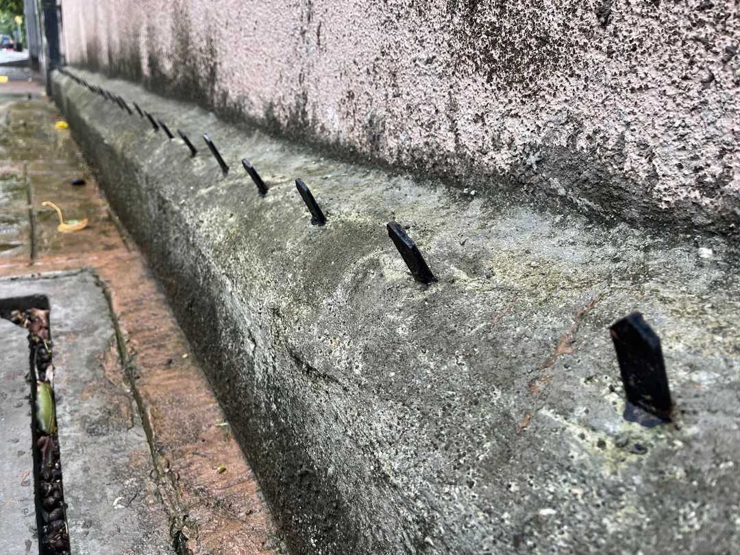 A rough concrete wall with sharp, black spikes protruding along its base exemplifies hostile architecture.