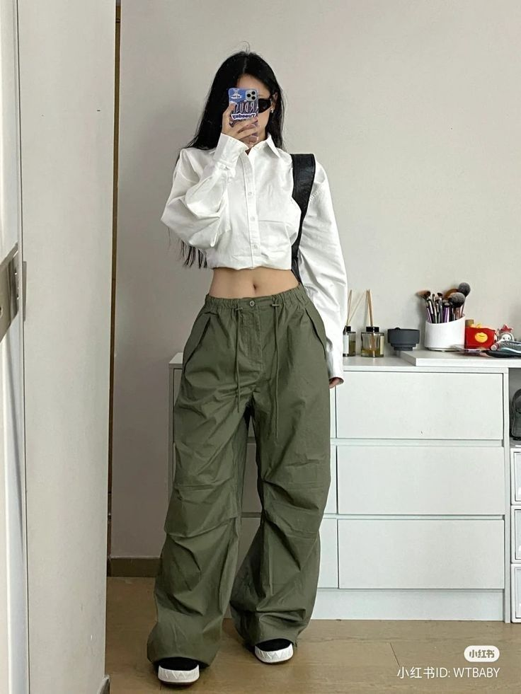 seorang wanita memakai cargo hijau, kemeja crop putih, dan sneaker hitam