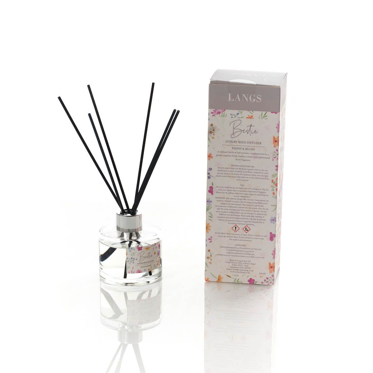 A Langs luxury reed diffuser set labeled "Bestie" in the scent Peony & Blush, featuring a clear glass bottle with black reeds and a floral-themed packaging box.
