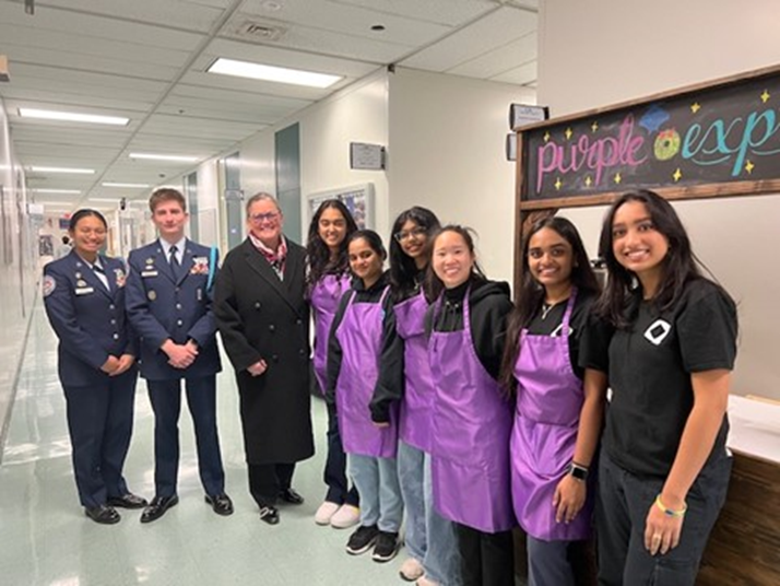 Dr. Reid with a group of students at Chantilly Academy, some are wearing military uniforms and others are wearing aprons. 