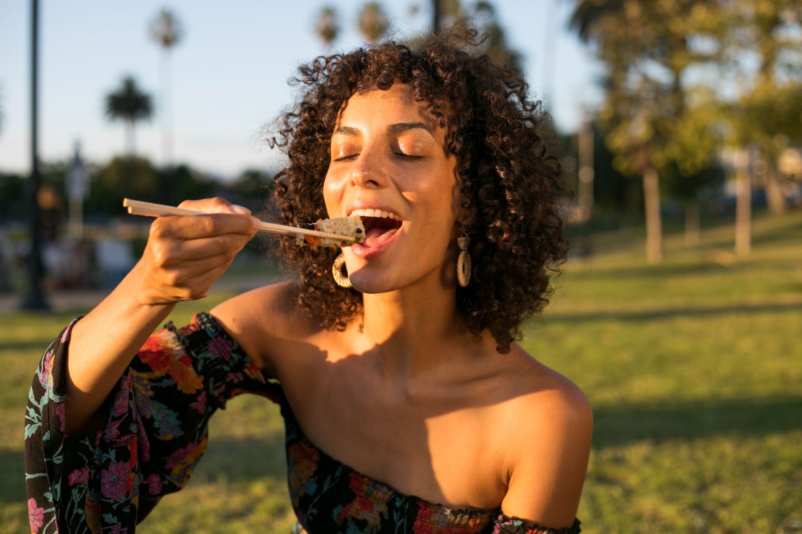 Woman using chopsticks to eat sushi outdoors. 