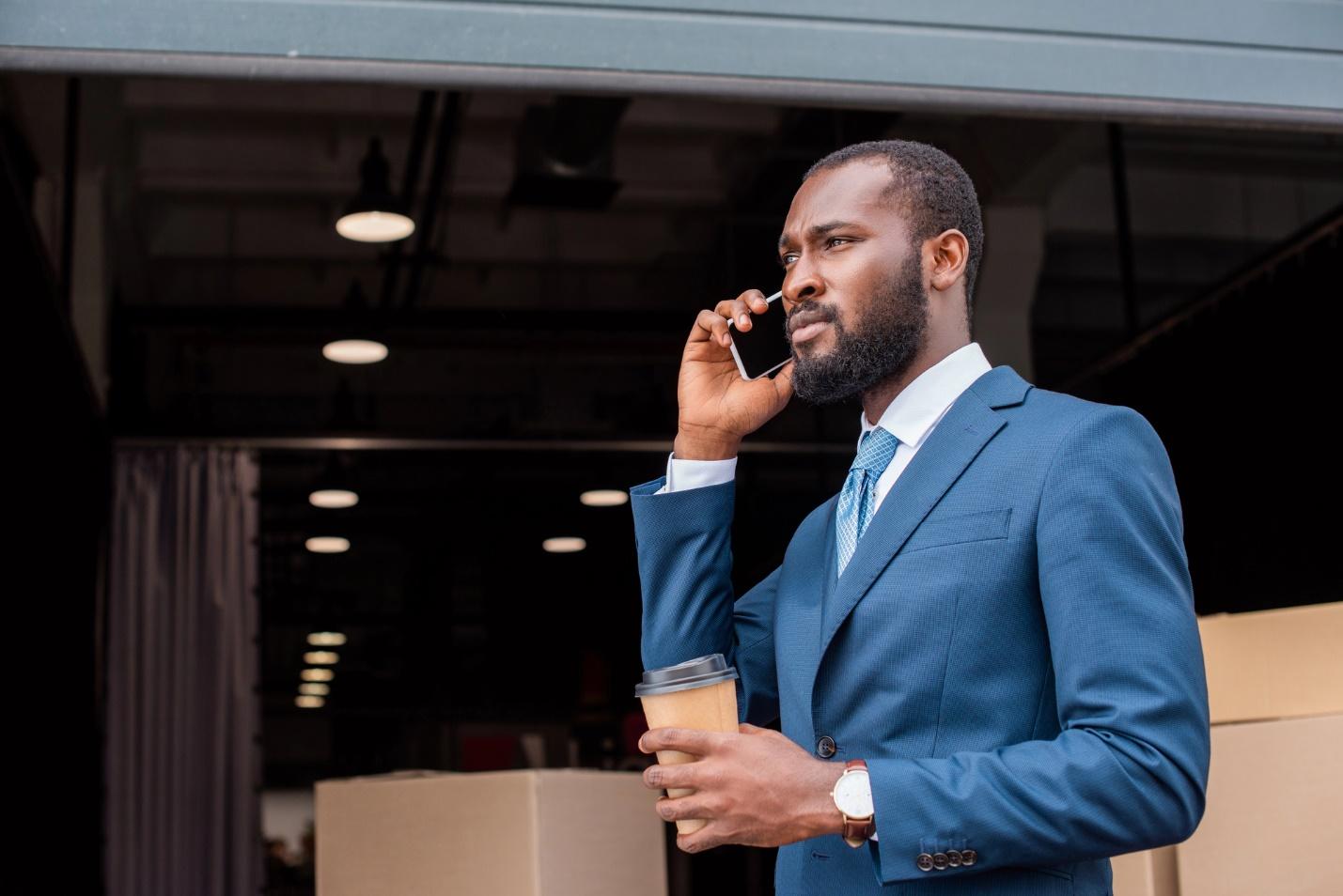 A person in a suit holding a coffee cup and talking on a cell phone

Description automatically generated