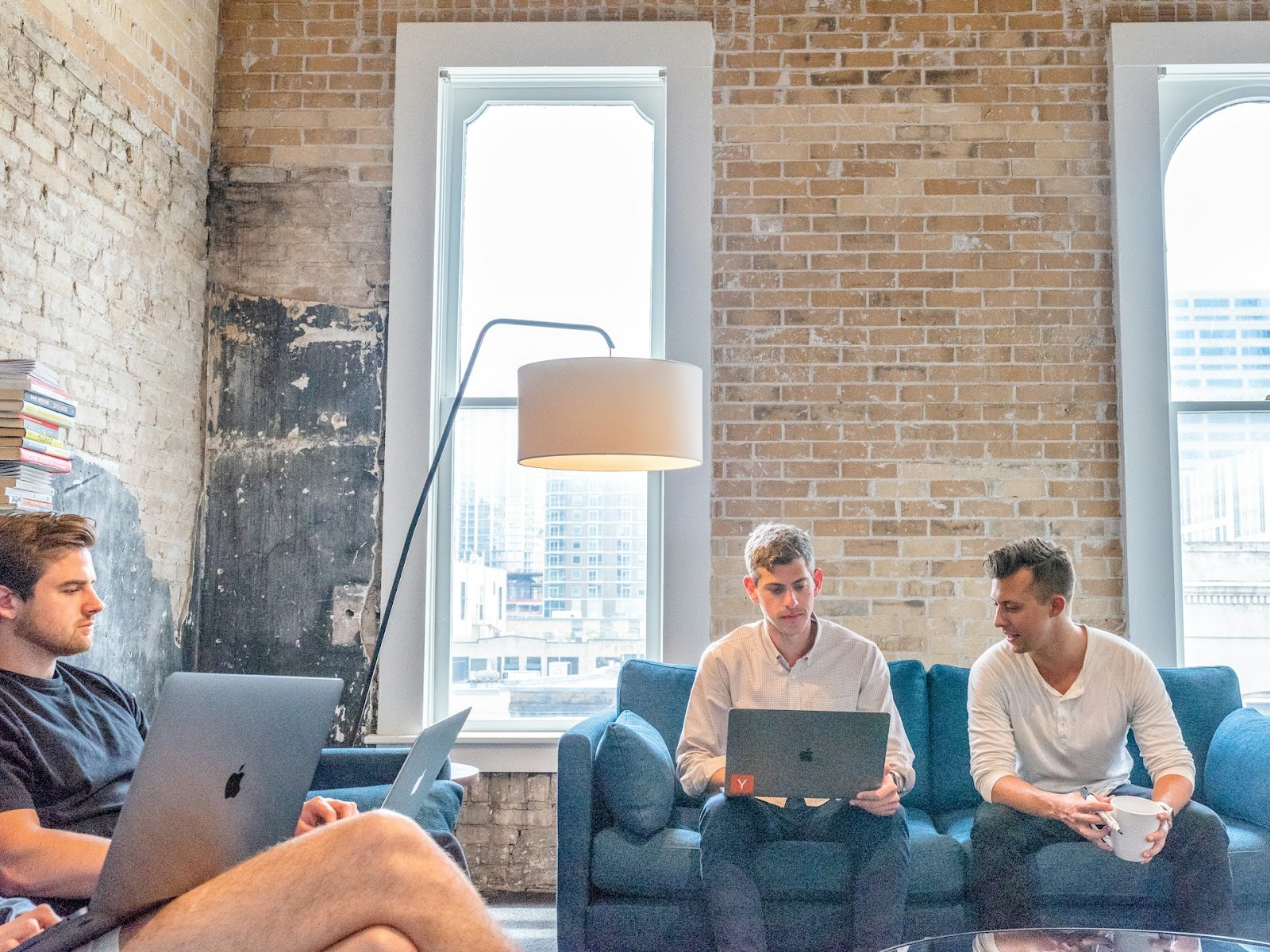 Three men casually sitting on couches, focused on their laptops, creating a relaxed and collaborative atmosphere.