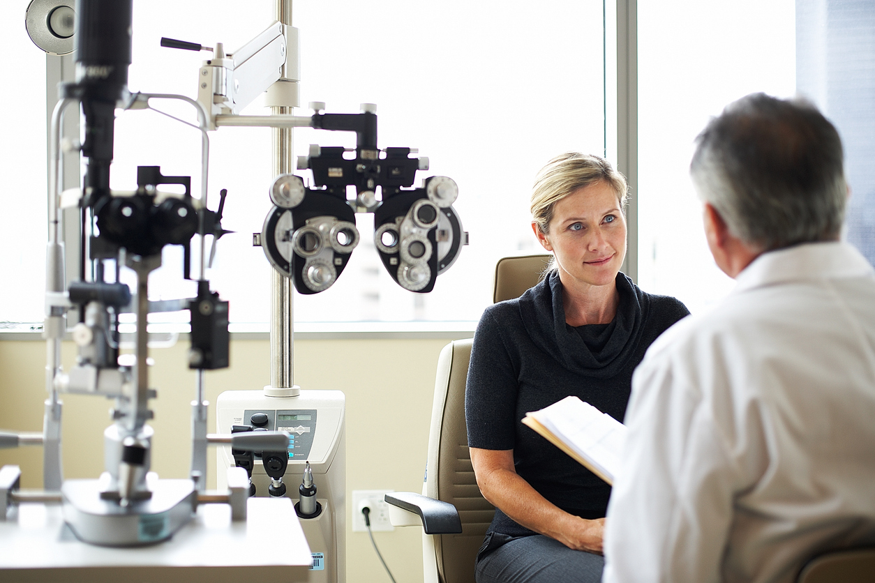 Women talking to her eye doctor in exam room with optometry diagnostic tools.