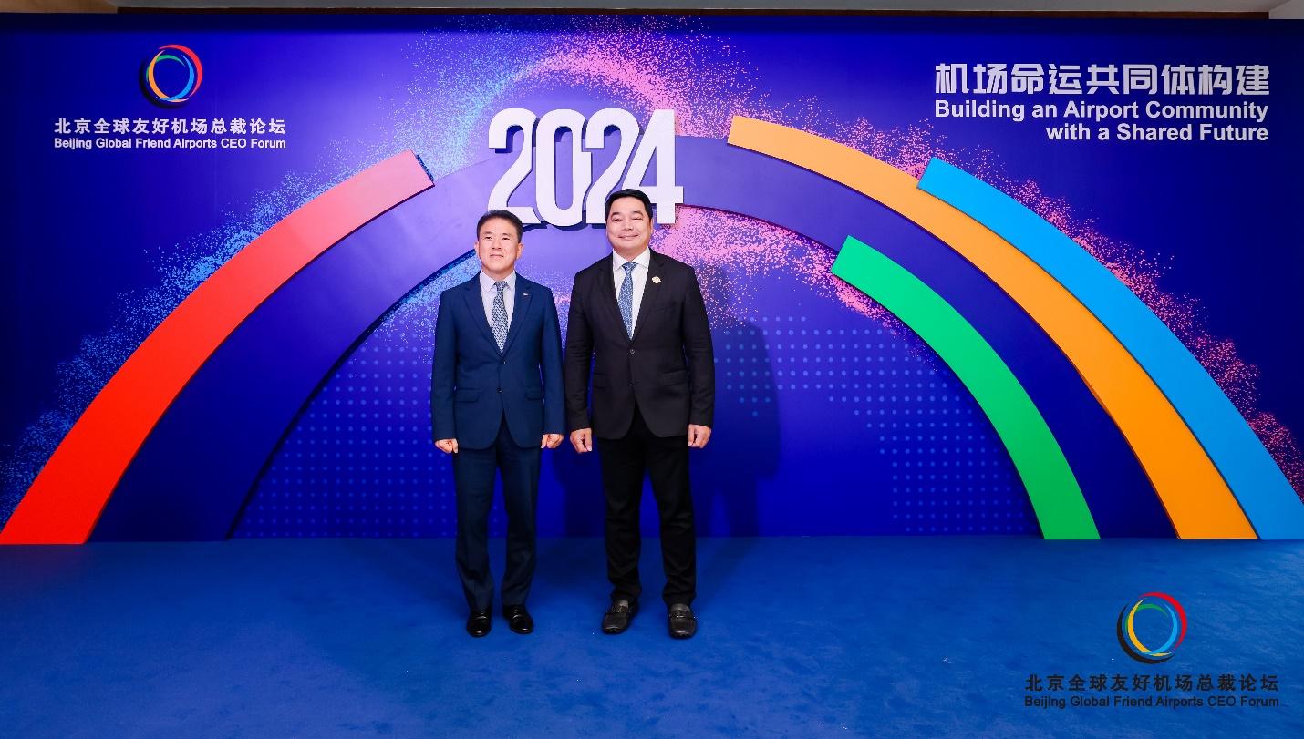 Two men standing in front of a blue wall with colorful rainbowsDescription automatically generated