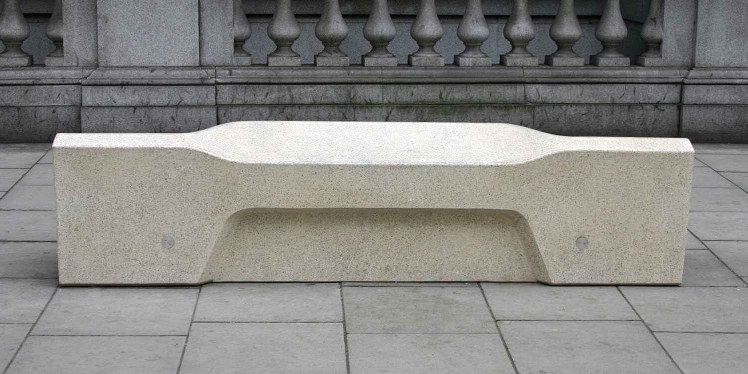 A modern concrete bench with a minimalist design set on a stone pavement showing hostile architecture in public spaces.