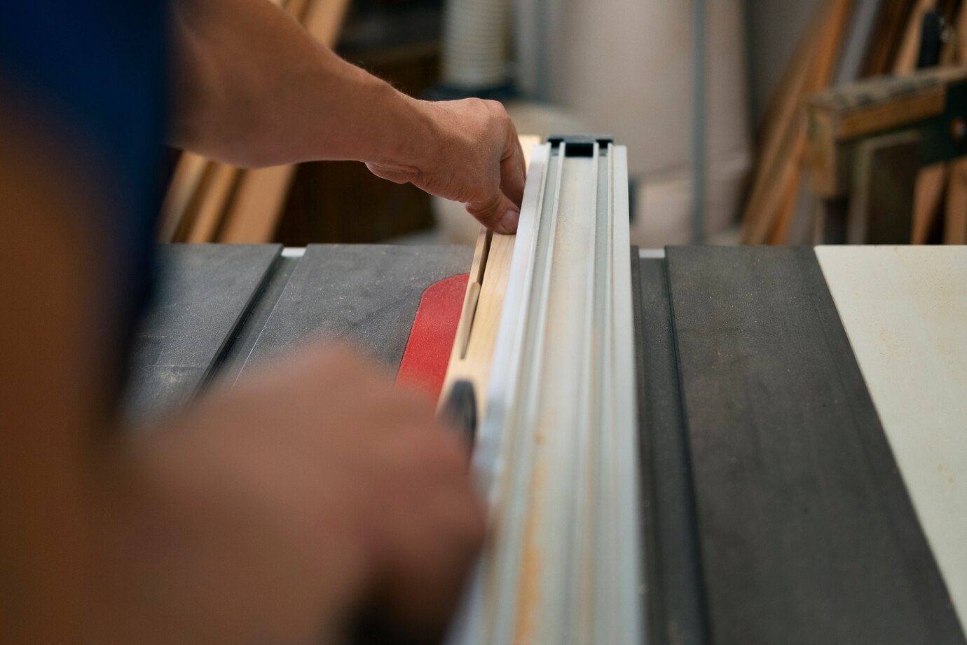 A person using a table saw in Garage Doors workshop to cut a wooden board, with a focus on precision and safety in a woodworking environment