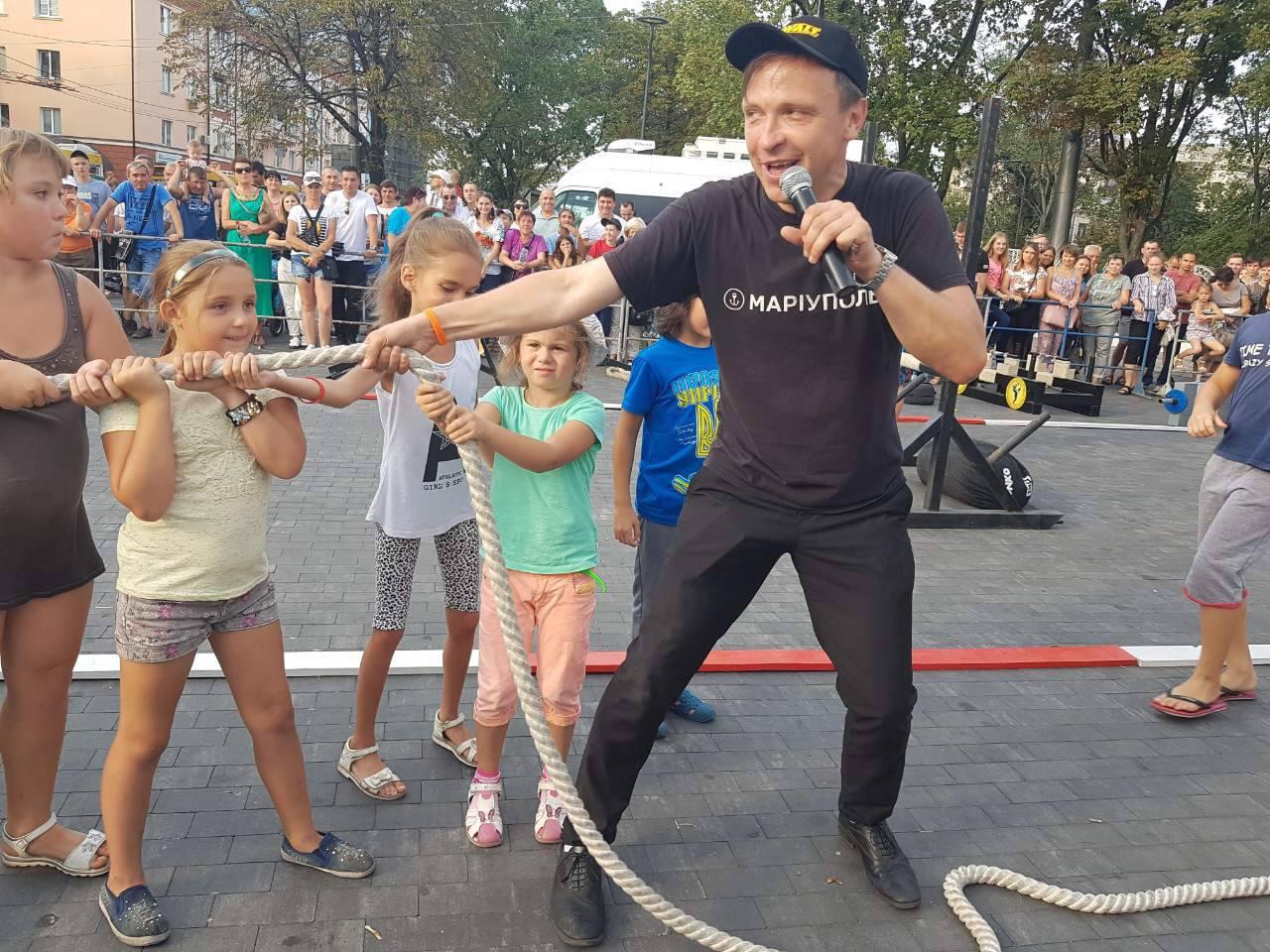 A person holding a microphone with a rope in front of a crowd

Description automatically generated