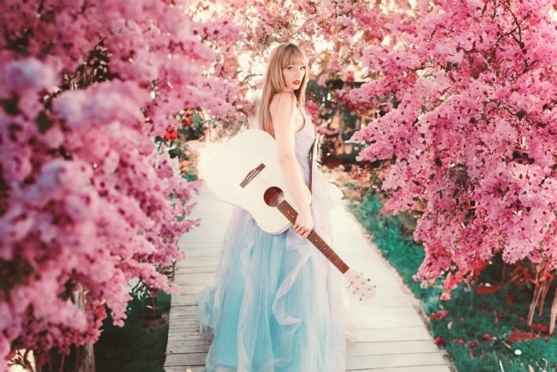 A person holding a guitar in front of pink flowers

Description automatically generated