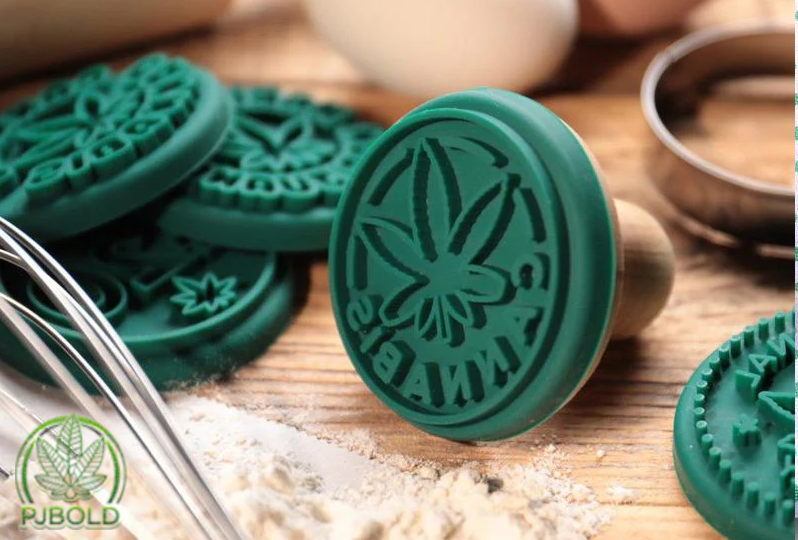 Green cannabis-themed cookie stamps and baking utensils on a wooden countertop