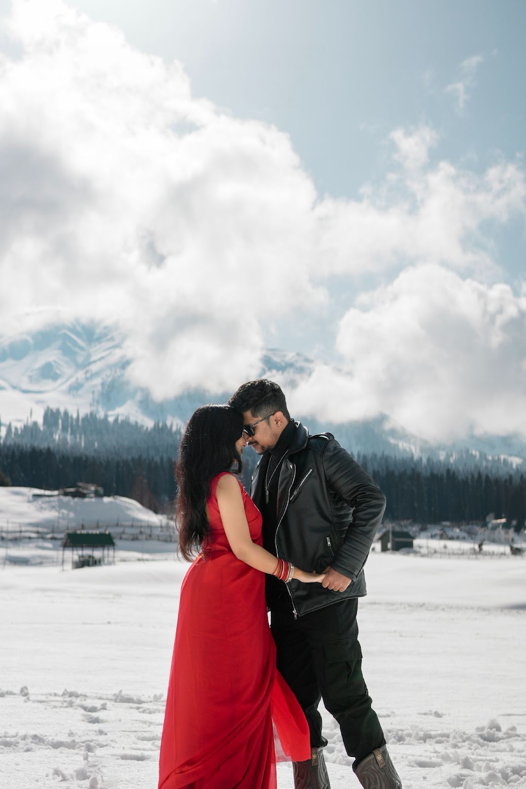 Pre-wedding photography in a winter wonderland, with a couple standing hand in hand on a snowy mountain