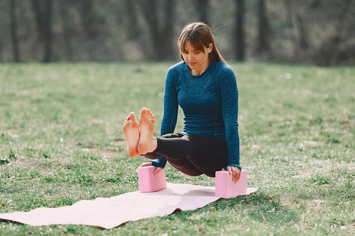 Foto de uma mulher a céu aberto fazendo yoga com dois blocos de yoga rosa em um gramado verde bonito.