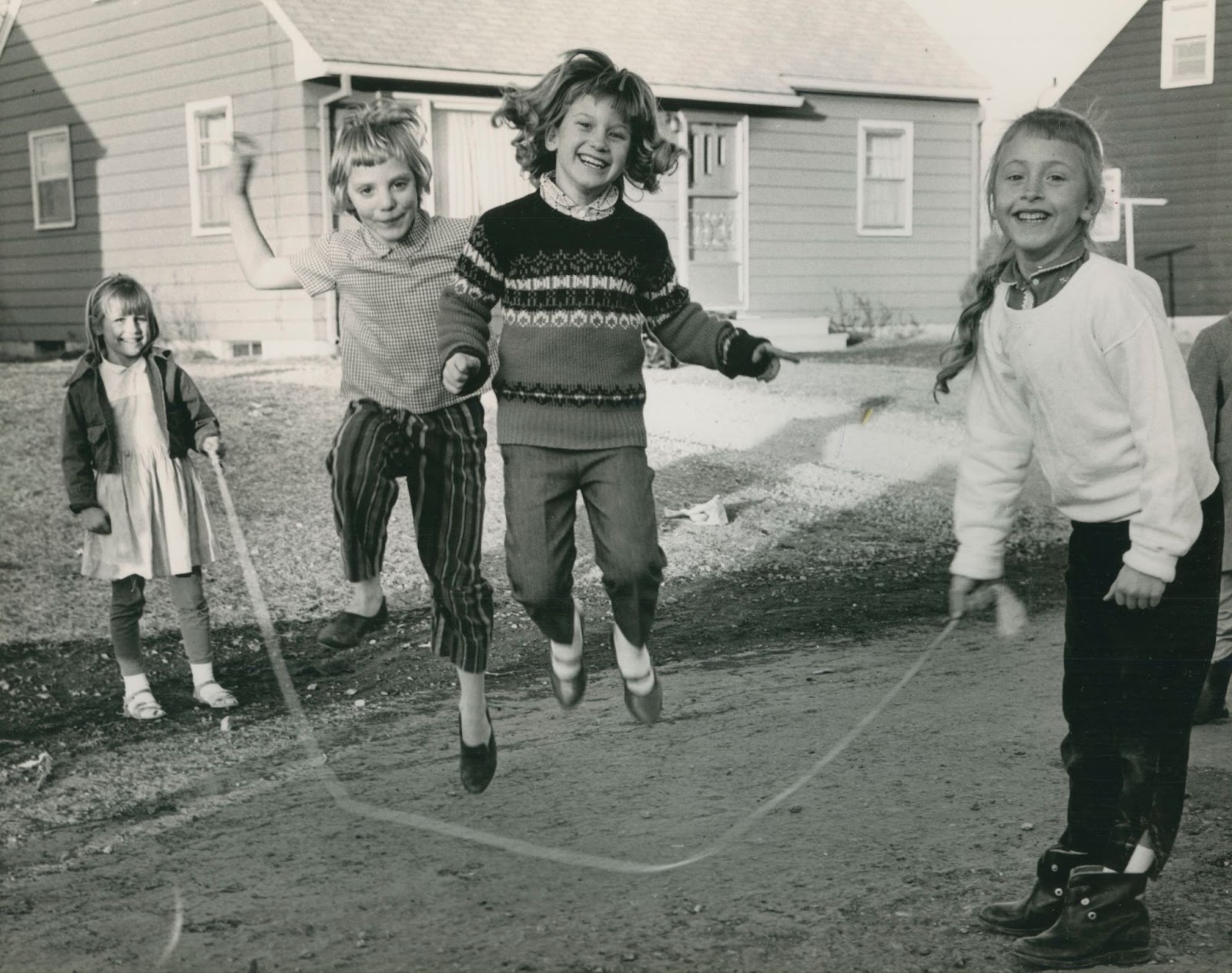 Four children play jump rope with two children jumping in the middle and two children holding either end of the rope. 