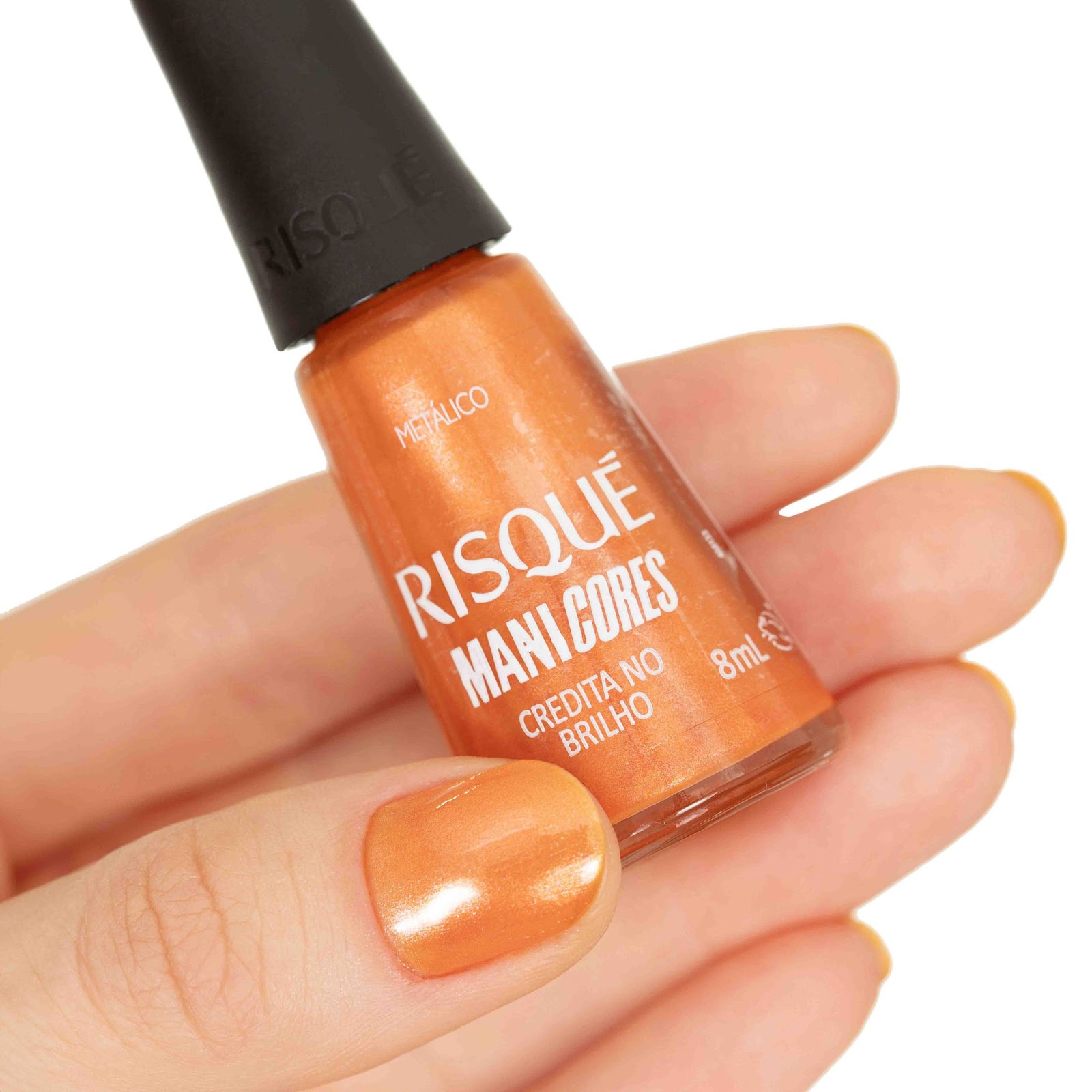 Uma mulher segura o esmalte Credita no Brilho com as unhas pintadas de laranja metálico.