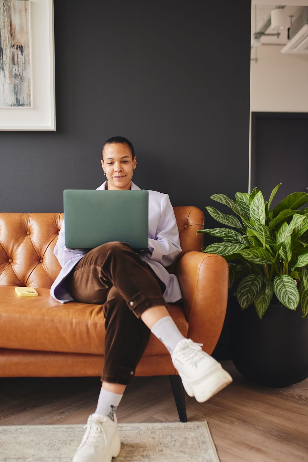 A person working with their laptop on a leather couch.