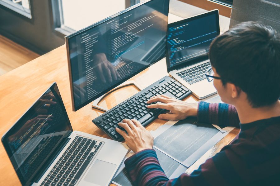 Person working on multiple computers with coding on screens.