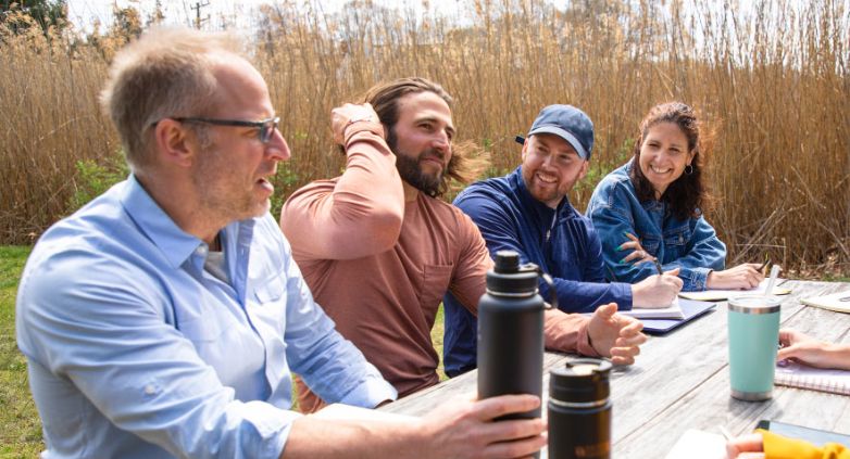 A group of people gathered around a picnic table, engaged in conversation, discussing support for a family member with addiction.
