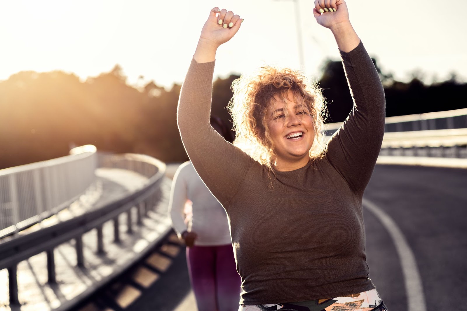 Woman in workout clothes walking with her hands in the air. 