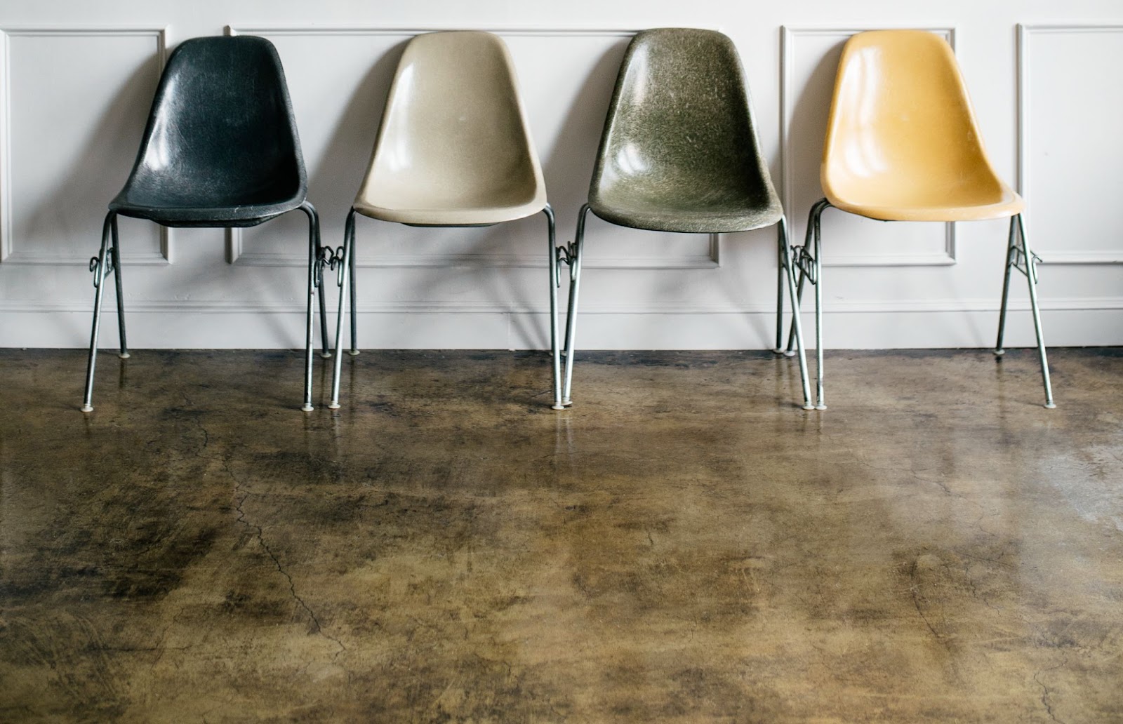  A well-polished concrete floor with four Eames-style chairs in different colors.