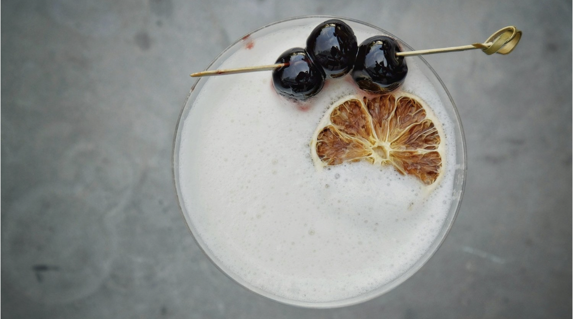 A sour cocktail is garnished with cherries and dehydrated citrus