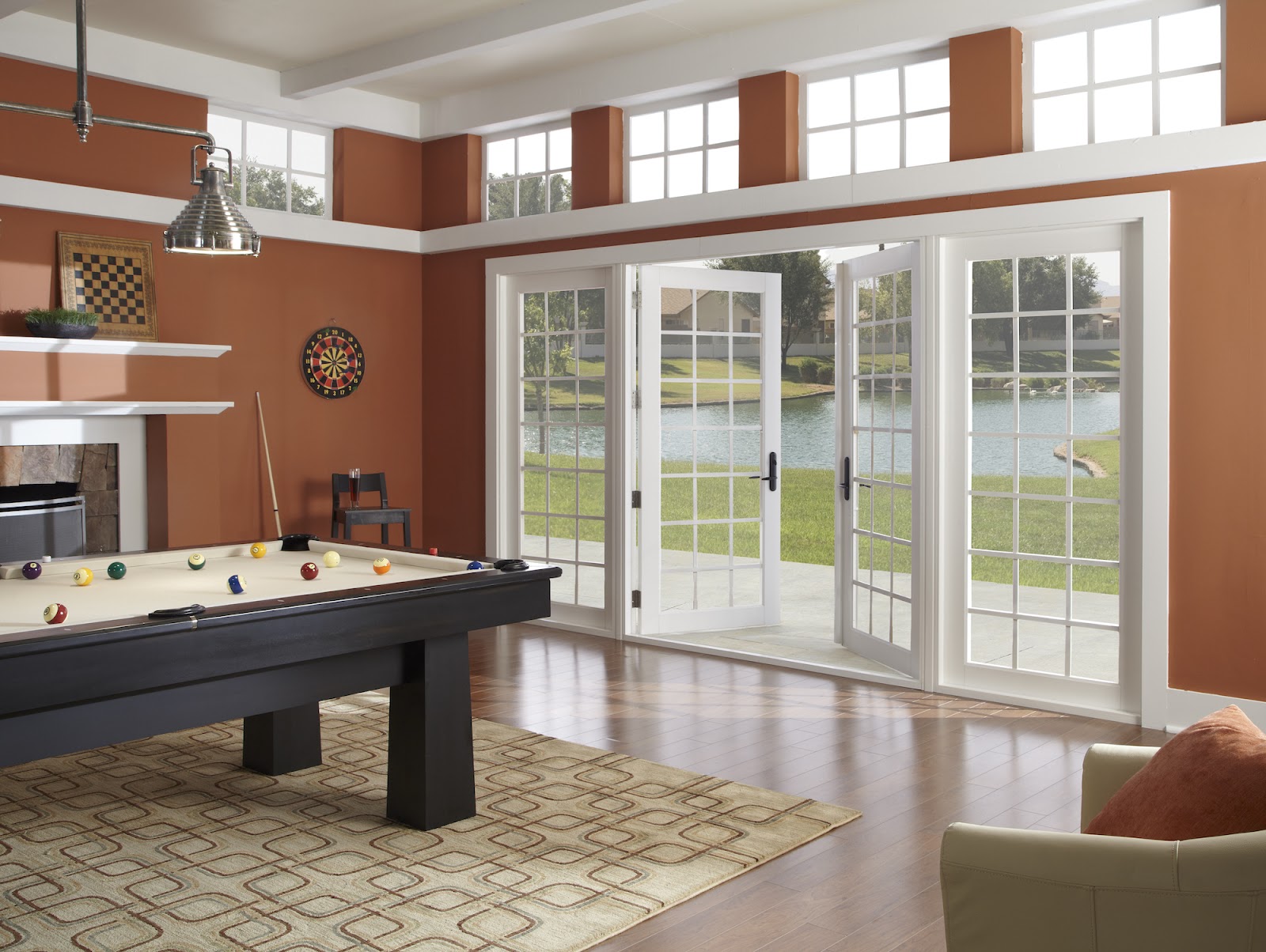 A game room with a pool table has two glass French doors that open to a backyard with a lake and are trendy.