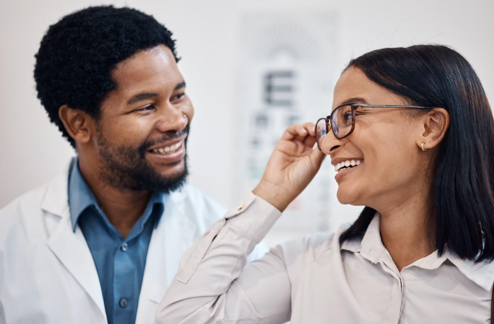 An optometrist helps a satisfied patient try on their new glasses after an eye exam.