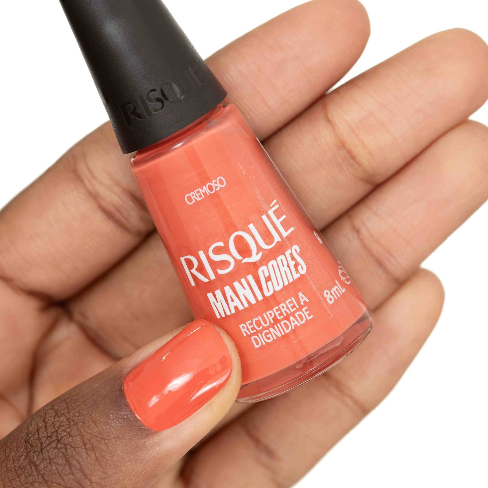 Uma mulher segura o esmalte Recuperei a Dignidade com as unhas pintadas de laranja.