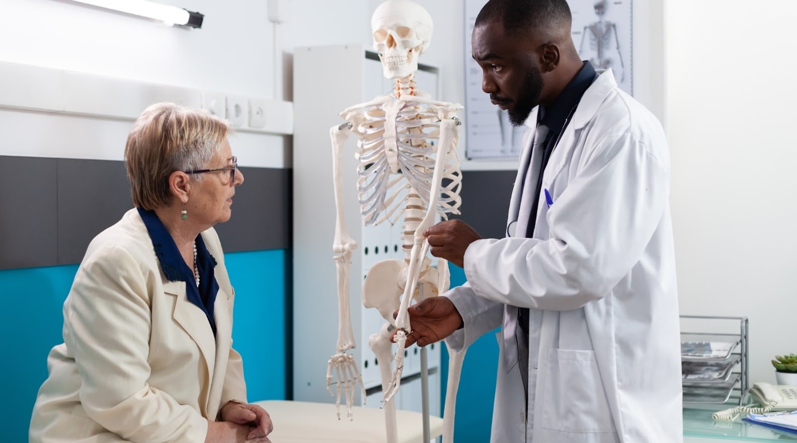 A dietitian is explaining the structure of a human skeleton to an elderly patient using an anatomical model.
