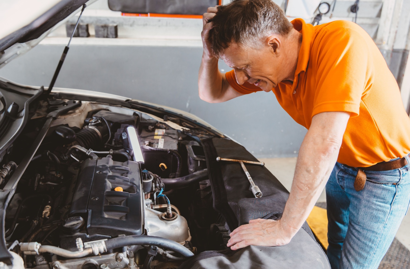 Car owner inspecting a car engine with a frustrated expression, holding his head.