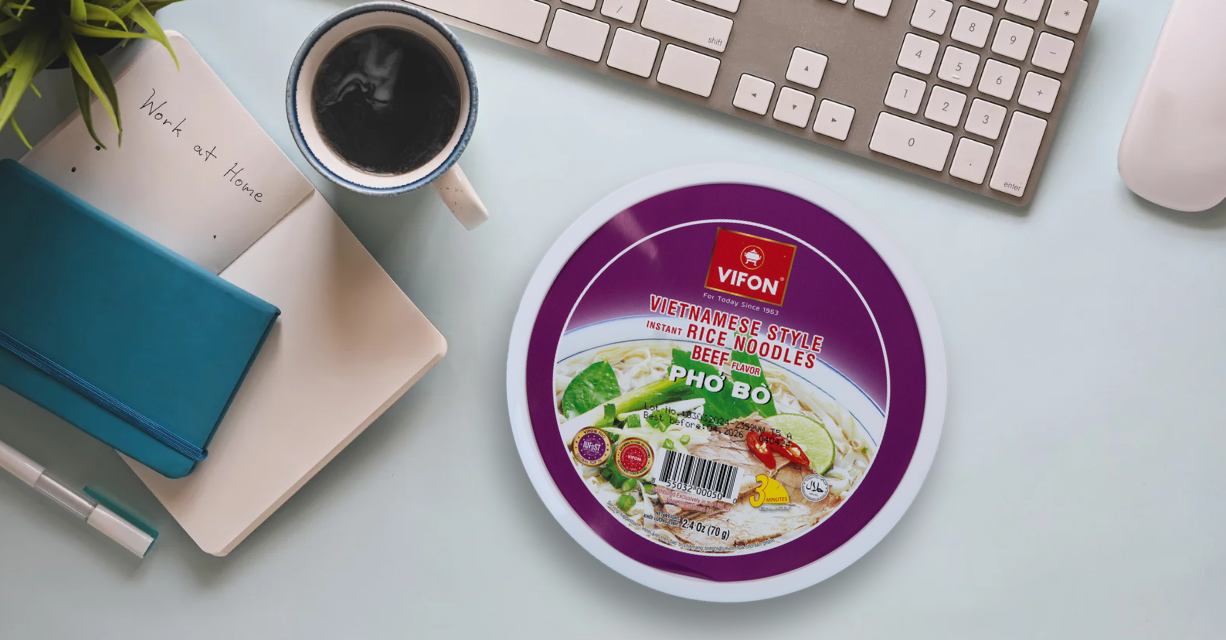 (Eine Schüssel Instant-Pho nach vietnamesischer Art von VIFON steht auf einem Schreibtisch neben einer Kaffeetasse, einer Tastatur und einem Notizbuch für die Arbeit von zu Hause.)