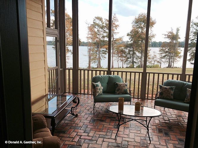The screened porch is furnished with cushioned chairs and glass top tables over terracotta tile flooring.