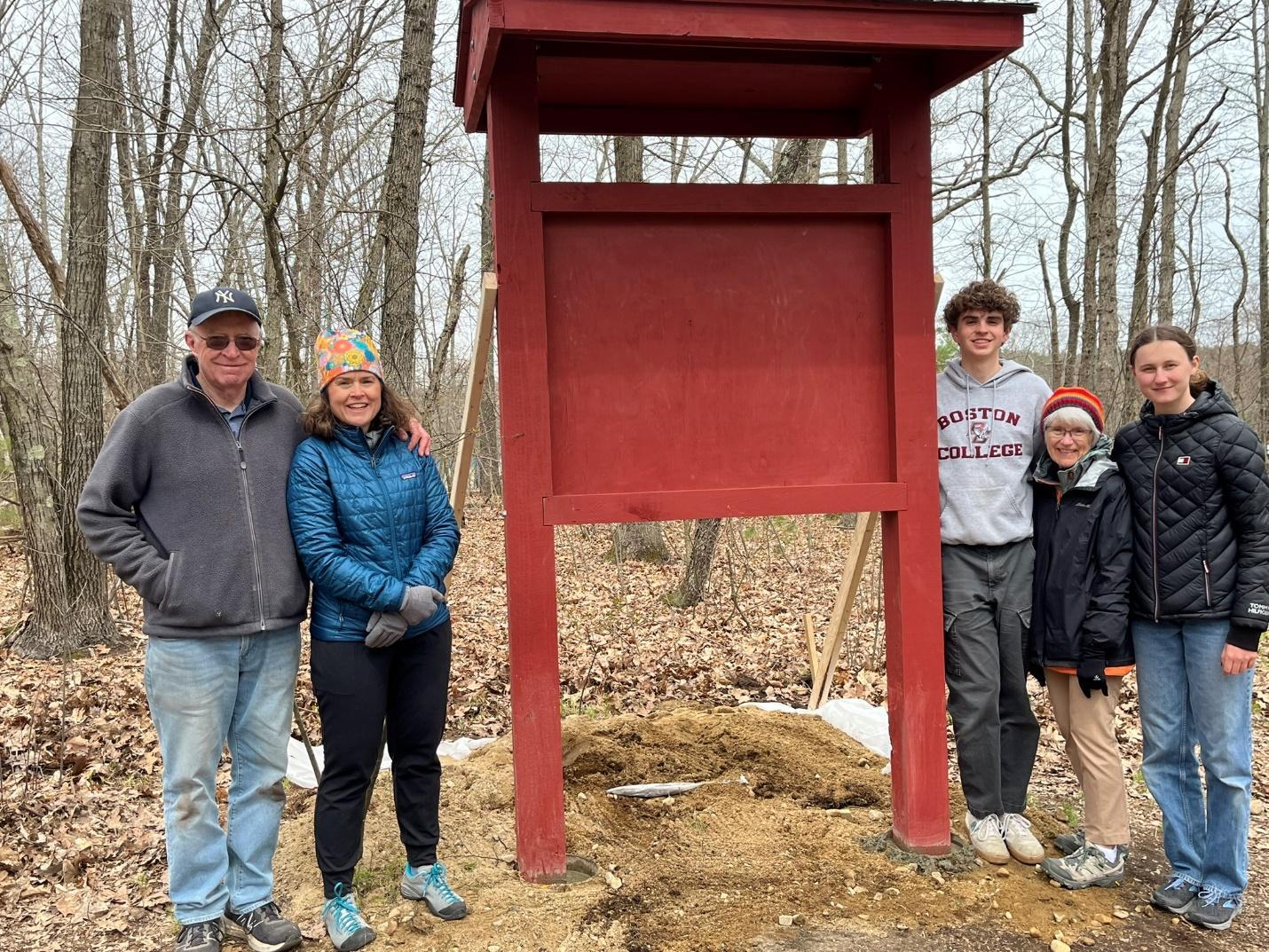 A group of people standing in front of a red sign

Description automatically generated