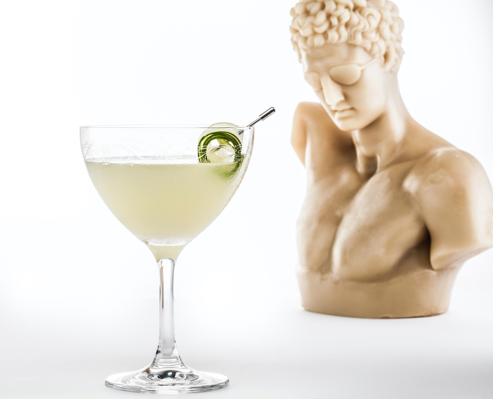 Lord Byron cocktail with cucumber in a coupe with a Greek bust in the background.