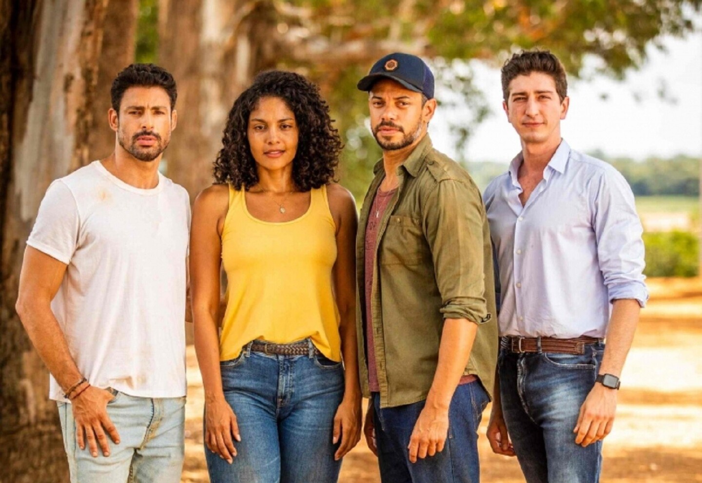 Cuatro personas de pie en un sendero arbolado, vistiendo ropa casual, posando juntos bajo la sombra de los árboles.